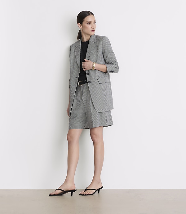 A woman in a black and white checkered blazer and shorts stands against a plain white background.