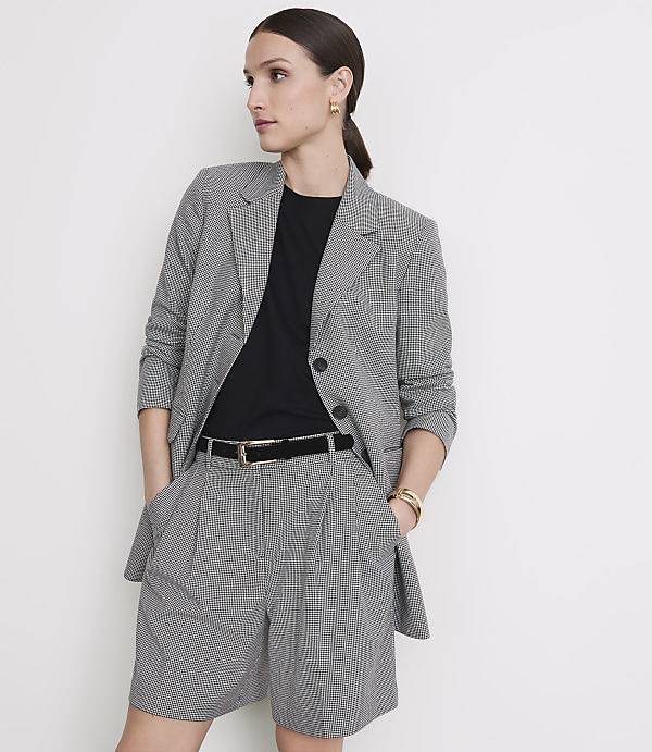 A woman in a black and white checkered blazer and shorts stands against a plain white background.