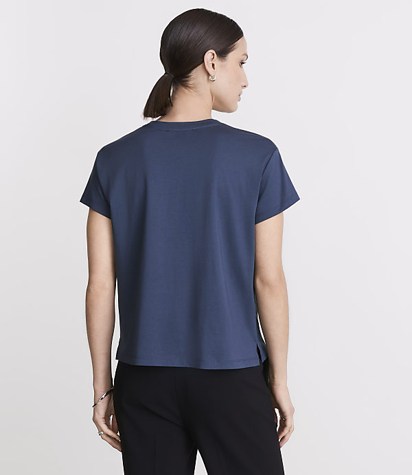 A woman in a blue t-shirt and black pants stands against a plain white background.