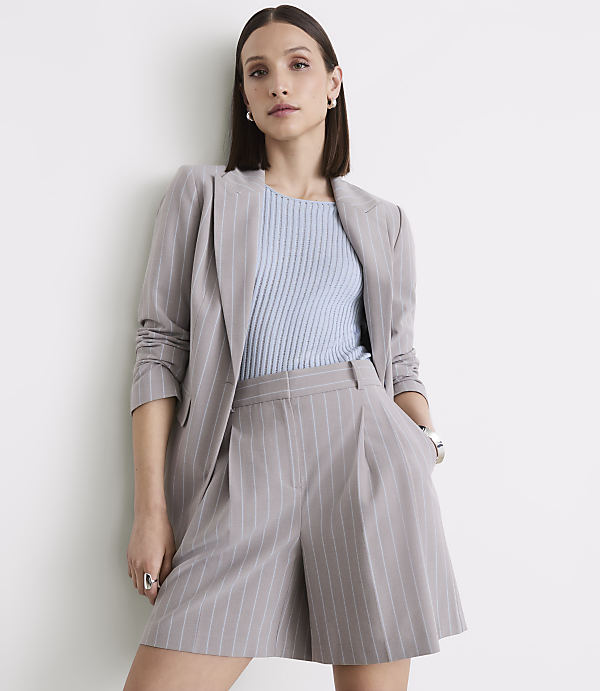 A woman in a pinstripe suit stands against a plain white wall.