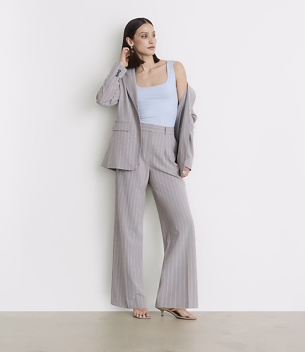 A woman in a light blue tank top and a pinstripe suit stands against a plain white wall.