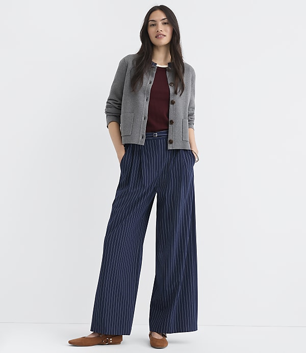 A woman in a gray cardigan and pinstripe pants stands against a plain white background.