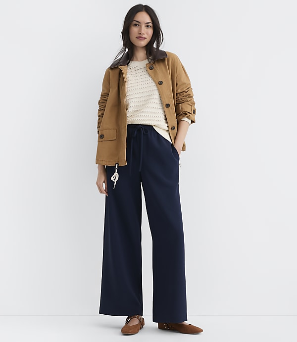 A woman in a brown jacket and navy pants stands against a plain white background.