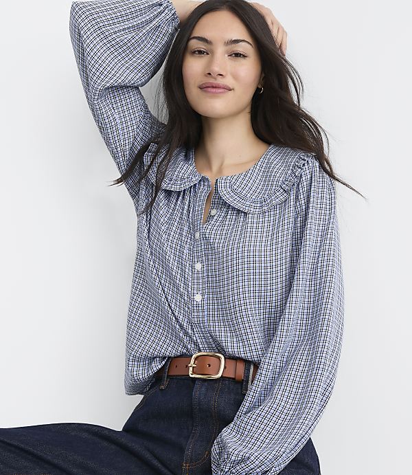 A woman in a blue gingham blouse and brown belt poses against a plain white background.