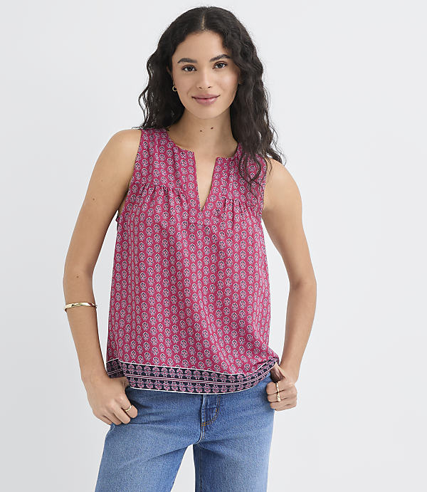 A woman in a patterned pink top and blue jeans stands against a plain white background.