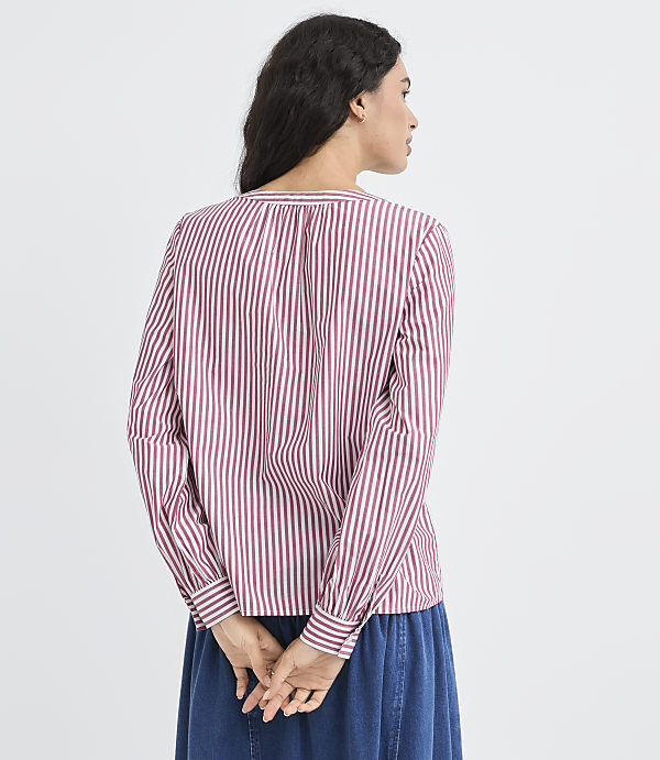 A woman in a striped shirt and blue skirt stands with her back to the viewer against a plain white background.