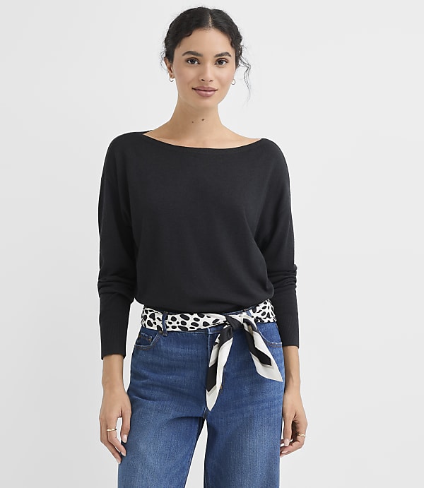 A woman in a black sweater and blue jeans stands against a plain white background.