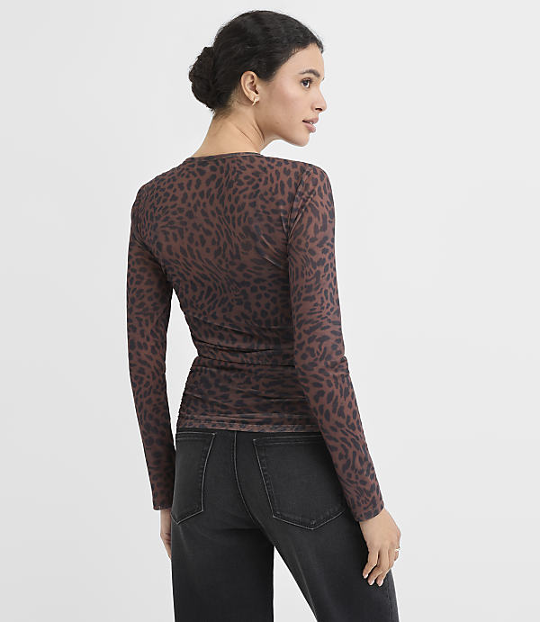 A woman in a leopard-print top and jeans stands against a plain background.
