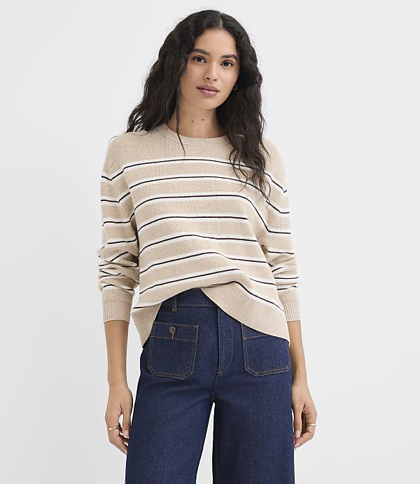 A woman in a striped sweater and dark denim pants stands against a plain white background.