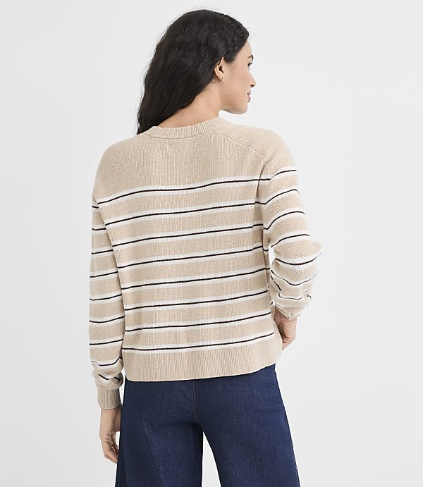 A woman in a striped sweater and dark pants stands against a plain, light background.