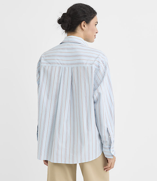 A woman in a light blue pinstripe shirt stands against a plain white background.