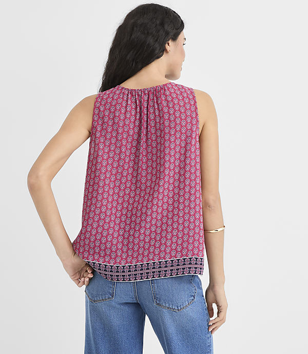 A woman in a patterned pink sleeveless top and blue jeans stands against a plain white background.