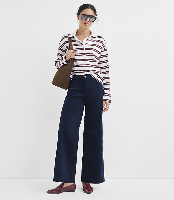 A woman in a striped shirt and wide-leg pants stands against a plain white background.