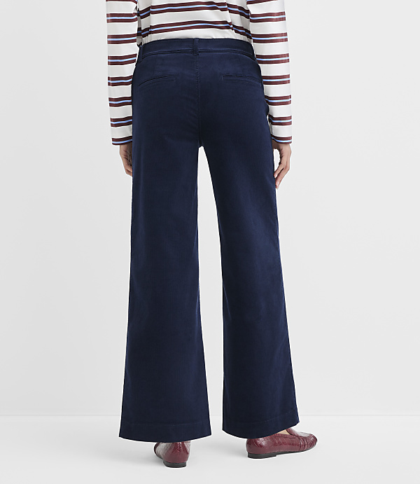 A person wearing dark blue wide-leg corduroy pants and a striped shirt stands against a plain white background.