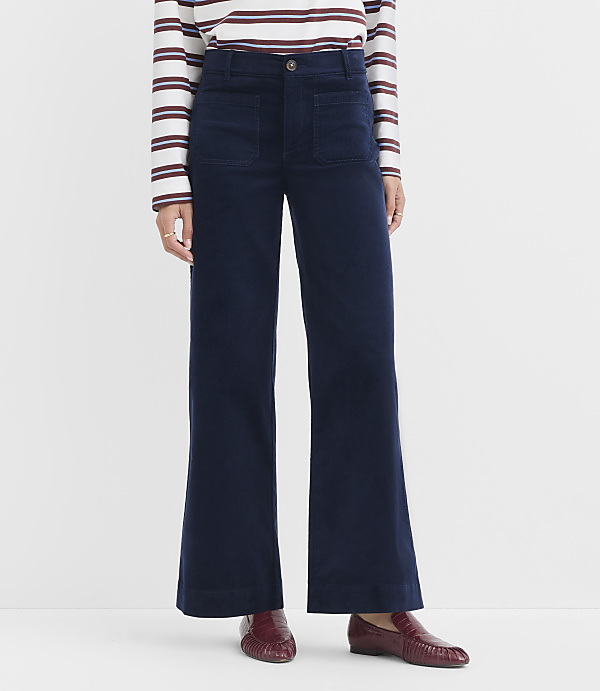 A person wearing navy wide-leg corduroy pants and a striped shirt stands against a plain white background.