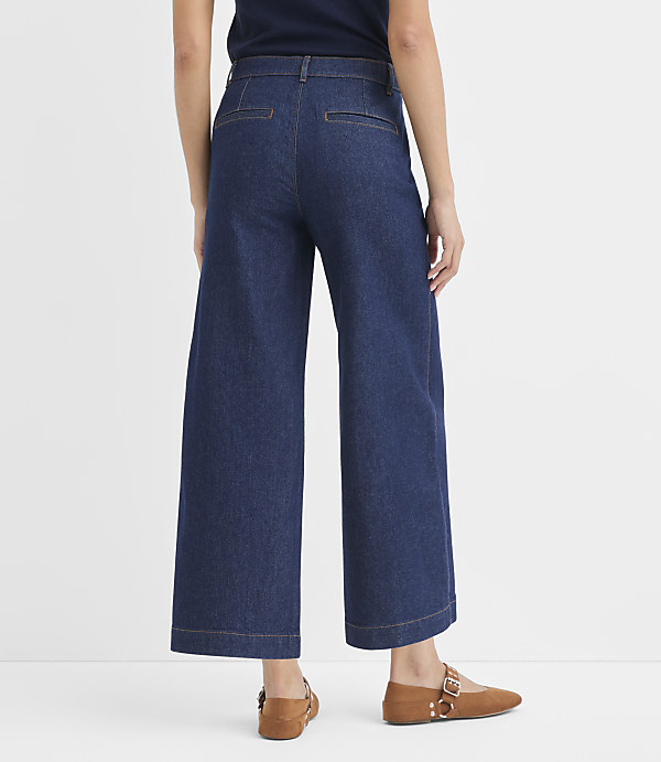 A person wearing dark wash wide-leg denim pants and brown loafers stands against a plain white background.