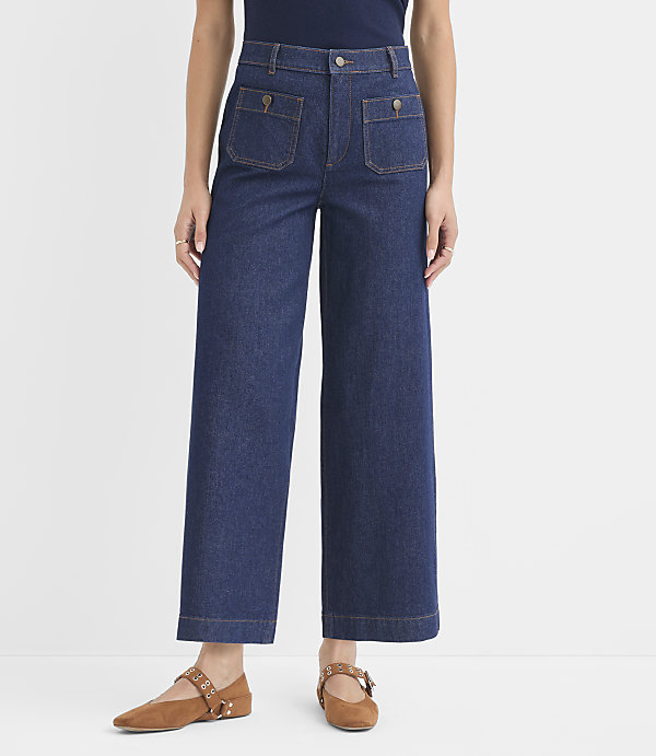 A person stands in dark wash wide-leg jeans with large front pockets and brown flats against a plain white background.