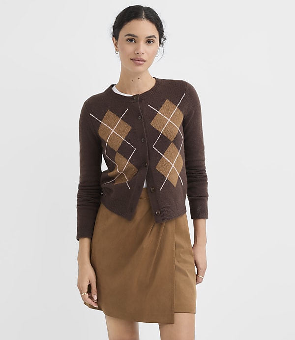 A woman in a brown argyle cardigan and a tan wrap skirt stands against a plain white background.