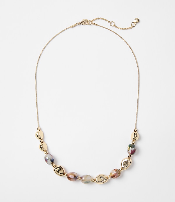 A delicate gold chain necklace with oval-shaped beads in earthy tones and gold accents rests on a plain white background.