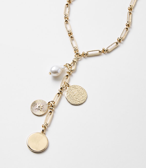 A gold necklace with a pearl and coin charms hangs against a plain white background.