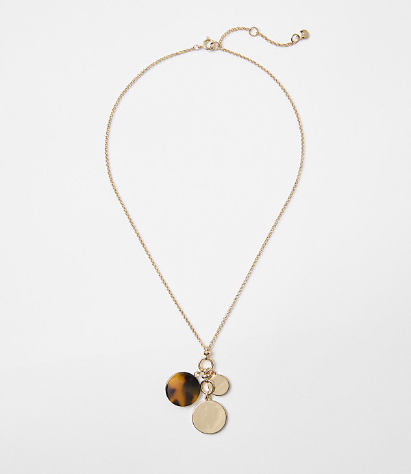 A delicate gold chain necklace with three circular pendants, one tortoiseshell and two gold, hangs against a plain white background.