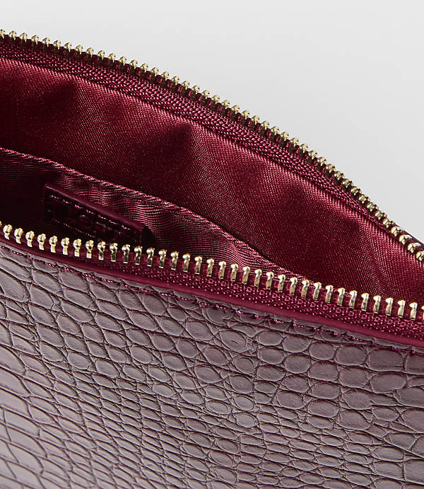A close-up of a burgundy embossed leather clutch with a gold zipper is set against a plain white background.