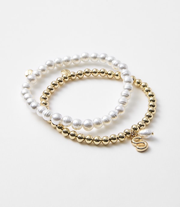 Two bracelets, one with pearls and the other with gold beads and an "S" charm, rest on a plain white background.