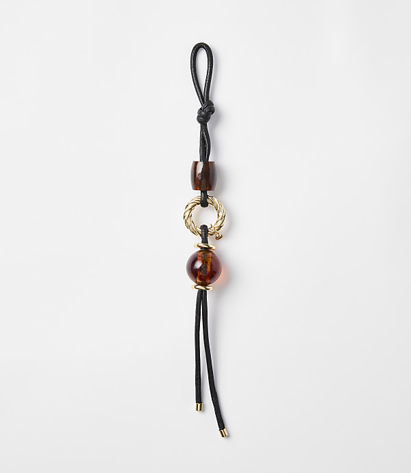 A black cord with amber-colored beads and a gold ring hangs against a plain white background.
