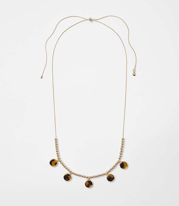 A delicate gold necklace with small beads and tortoise shell pendants hangs against a plain white background.