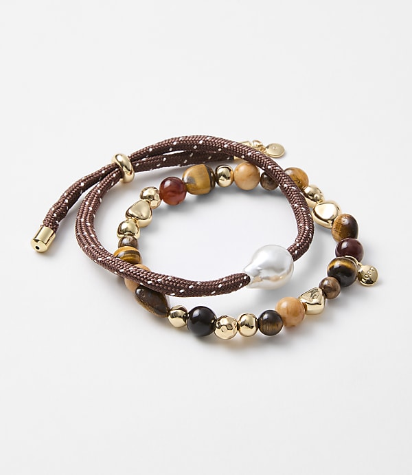 Two beaded bracelets, one with a large pearl and the other with various stones and gold accents, are arranged on a plain white background.
