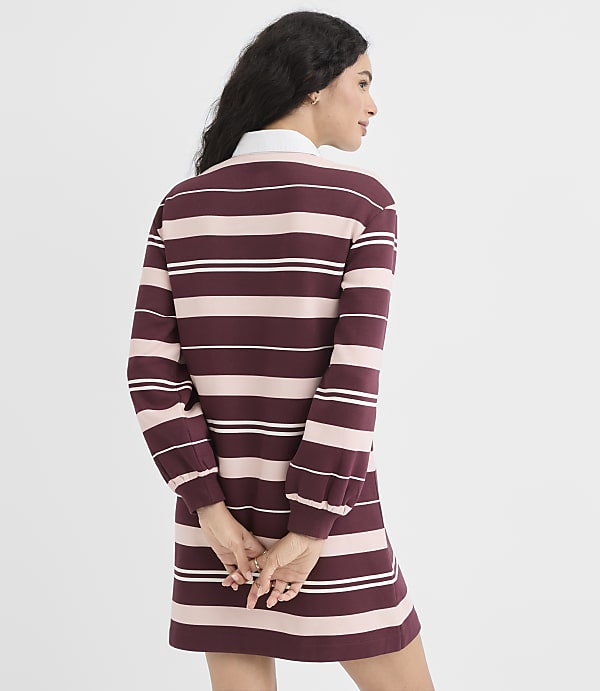 A woman in a striped dress stands against a plain white background.
