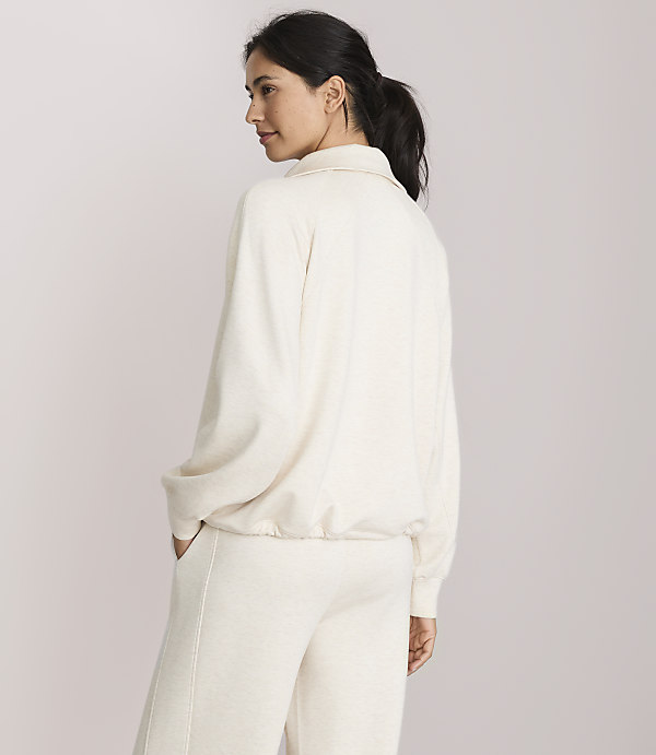 A woman in a cream-colored tracksuit stands with her back to the viewer against a plain, light background.