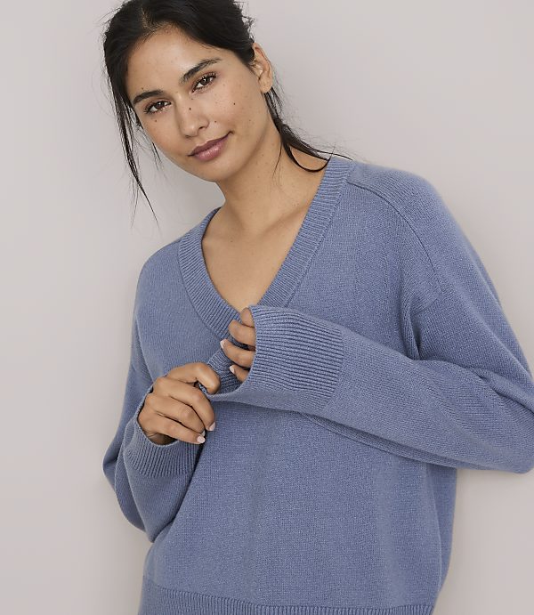 A woman in a blue v-neck sweater poses against a plain, light gray background.