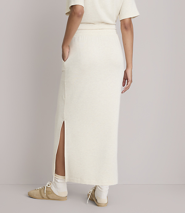 A person wearing a cream-colored knit skirt with a side slit and sneakers stands against a plain white background.