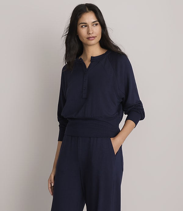 A woman in a navy blue henley shirt and matching pants stands against a plain gray background.