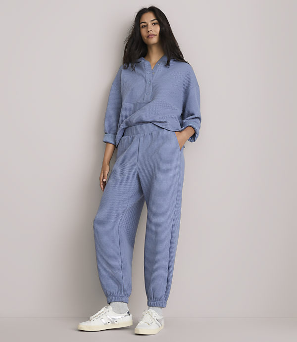 A woman in a blue loungewear set stands against a plain, light gray background.