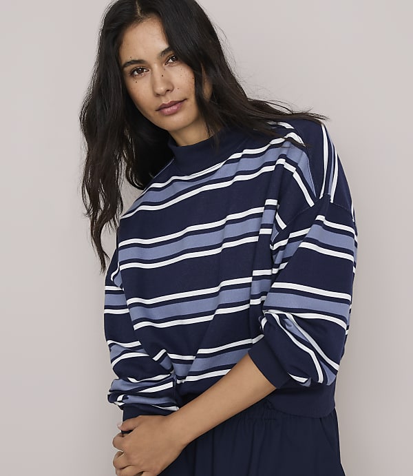 A woman with dark hair and a striped sweater is posed against a plain gray background.