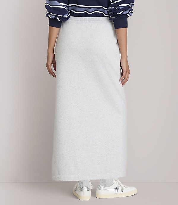 A person wearing a light gray maxi skirt and a striped sweater stands against a plain background.