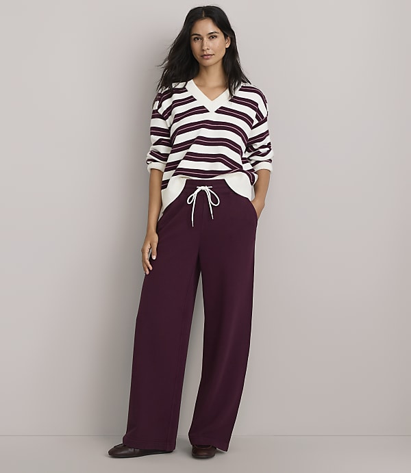 A woman in a striped sweater and wide-leg burgundy pants stands against a plain gray background.