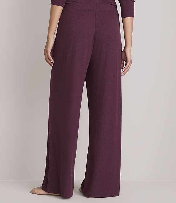 A person wearing plum-colored wide-leg pajama pants stands against a plain gray background.
