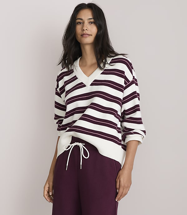 A woman in a striped sweater and maroon sweatpants stands against a plain, light gray background.