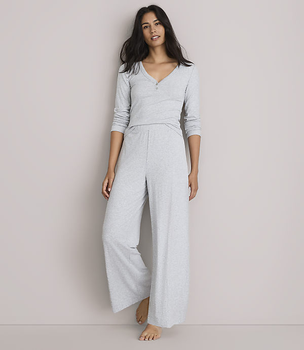 A woman in light gray pajamas stands against a plain, light gray background.