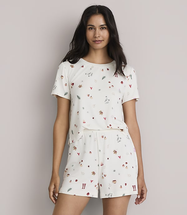 A woman in a cream-colored pajama set with a scattered pattern of small festive icons stands against a plain, light-colored background.