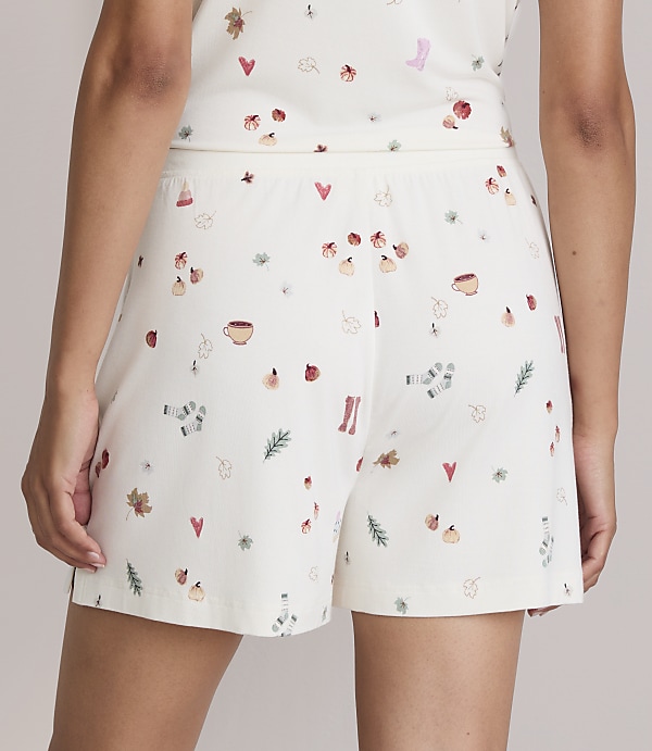 A person wears cream-colored shorts with a pattern of autumn-themed icons, set against a plain, light background.