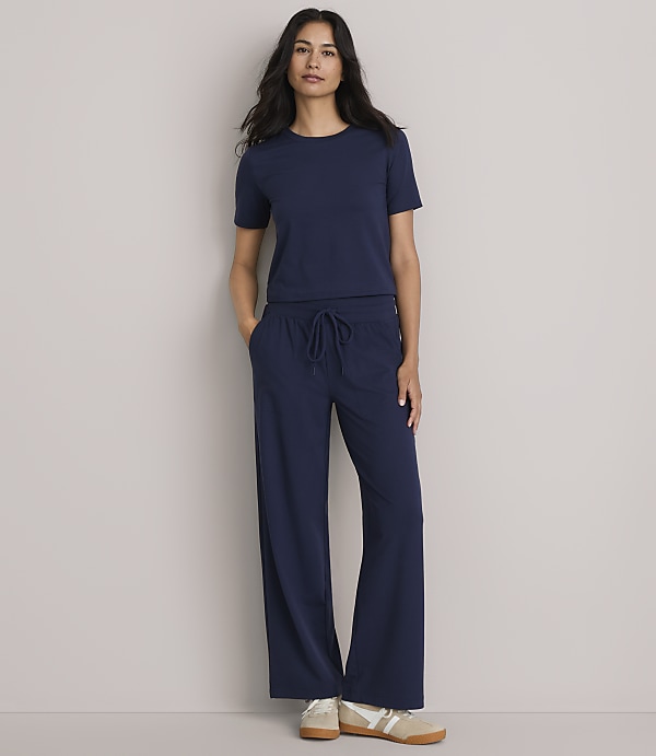 A woman in a navy blue t-shirt and wide-leg pants stands against a plain gray background.