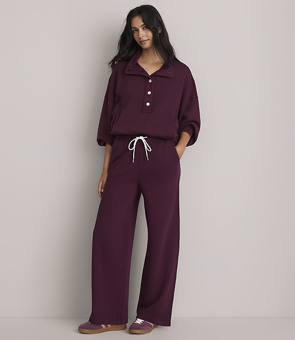 A woman in a burgundy loungewear set stands against a plain gray background.