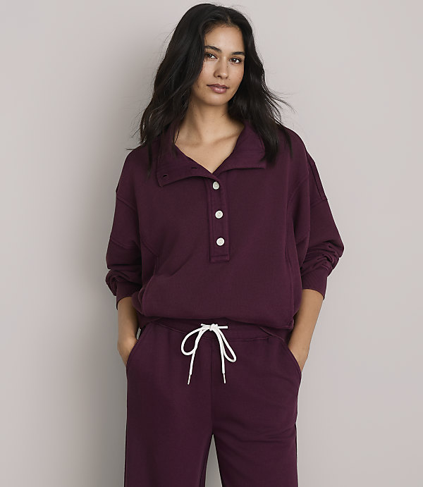 A woman in a burgundy sweatshirt and sweatpants stands against a plain gray background.