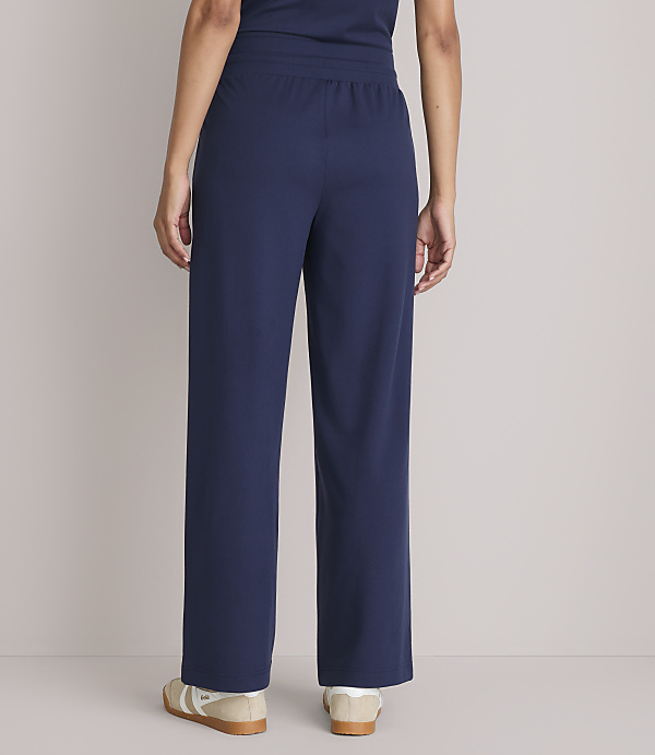 A person wearing navy blue pajama pants and sneakers stands against a plain gray background.