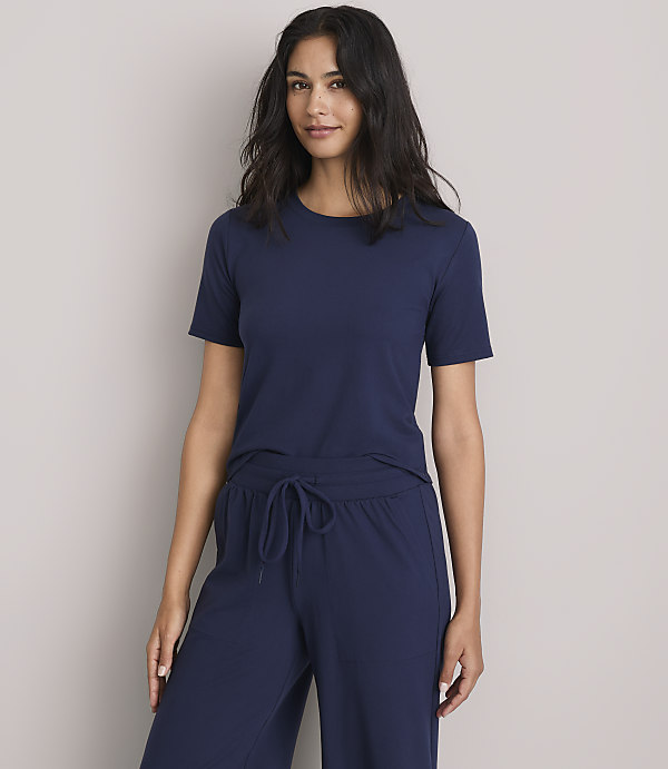 A woman in a navy blue t-shirt and matching pants stands against a plain gray background.