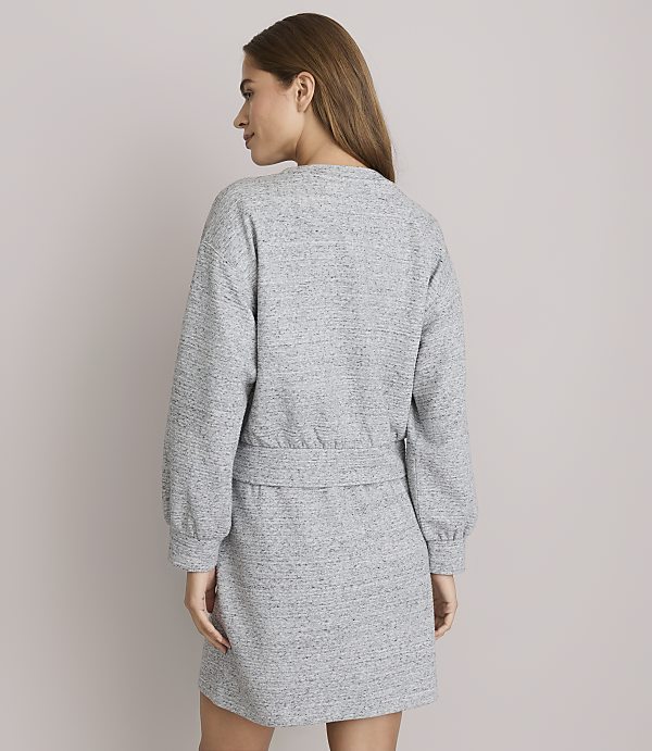 A woman in a grey dress stands against a plain grey background.